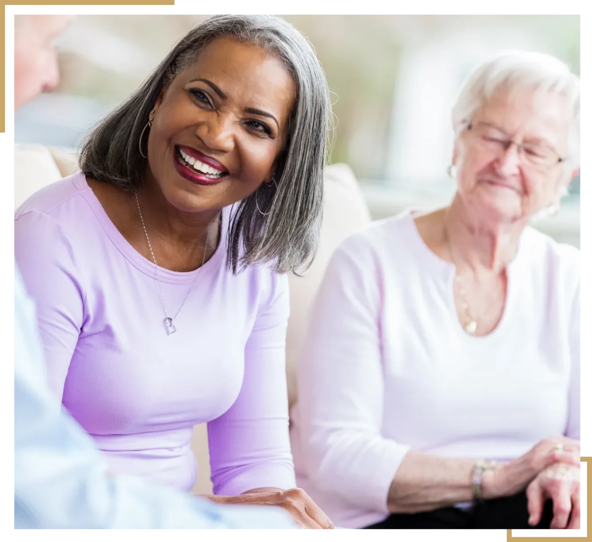 Two women smiling and conversing on couch.
